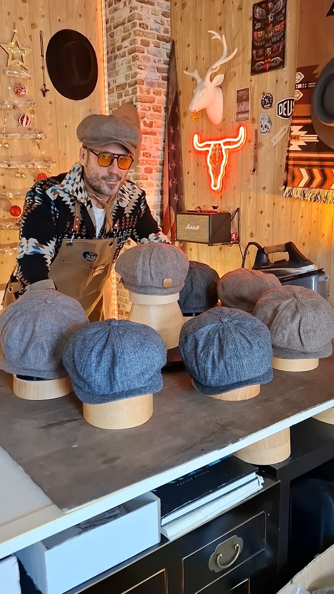 Artesano con gorra newsboy tras una mesa con boinas expuestas en el taller